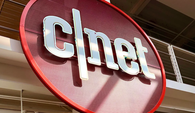 CNET homepage displayed on a tablet screen surrounded by smartphones and gadgets