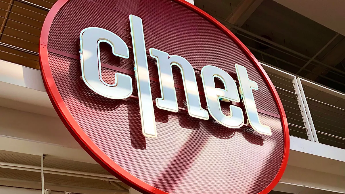 CNET homepage displayed on a tablet screen surrounded by smartphones and gadgets